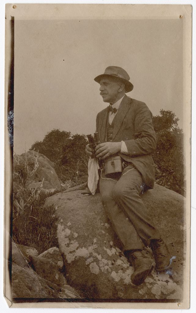 Godfrey Rivers, seated on a rock with binoculars