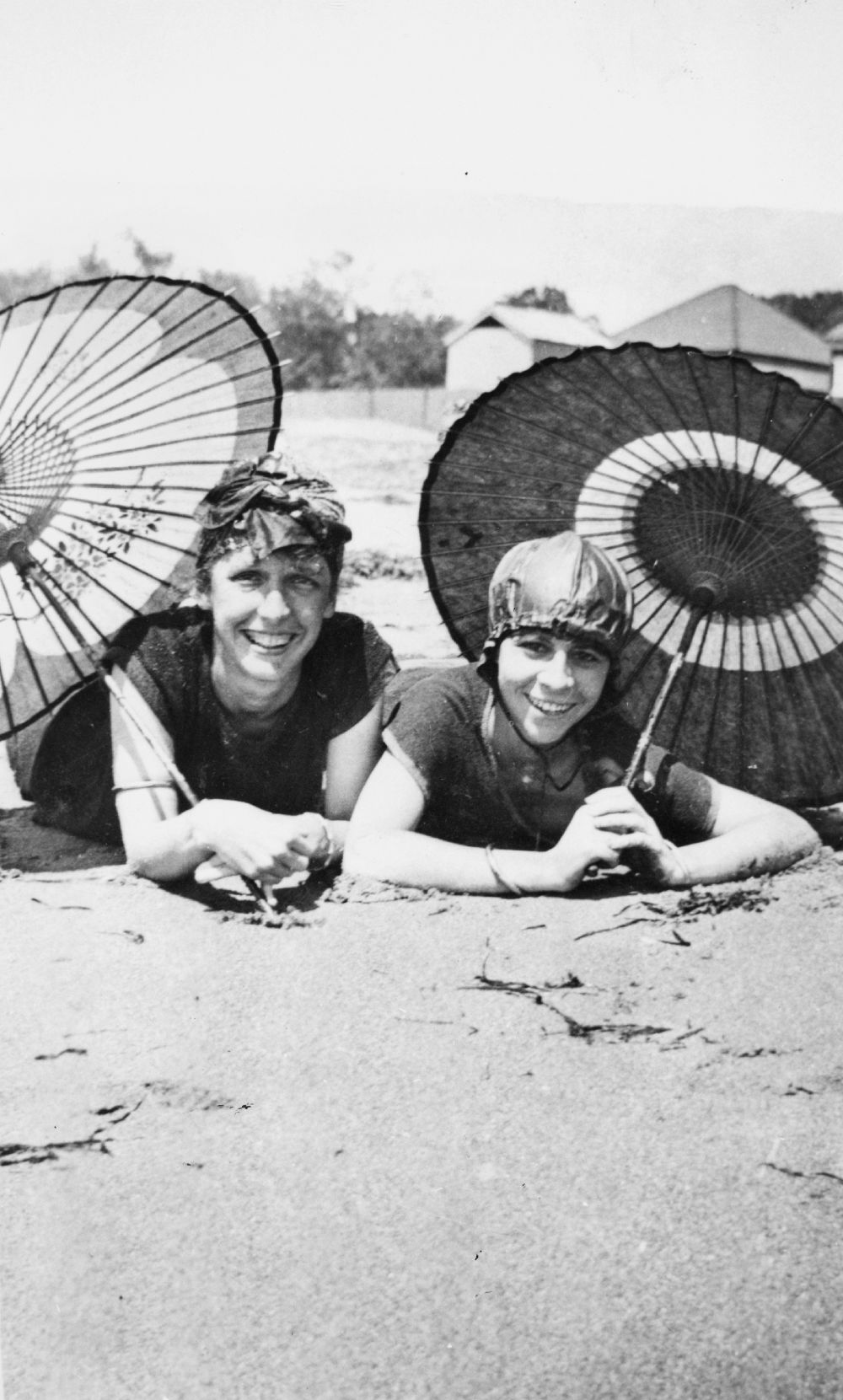 Two young ladies relaxing in the sun under parasols at Sutton's Beach, Redcliffe, 1919
